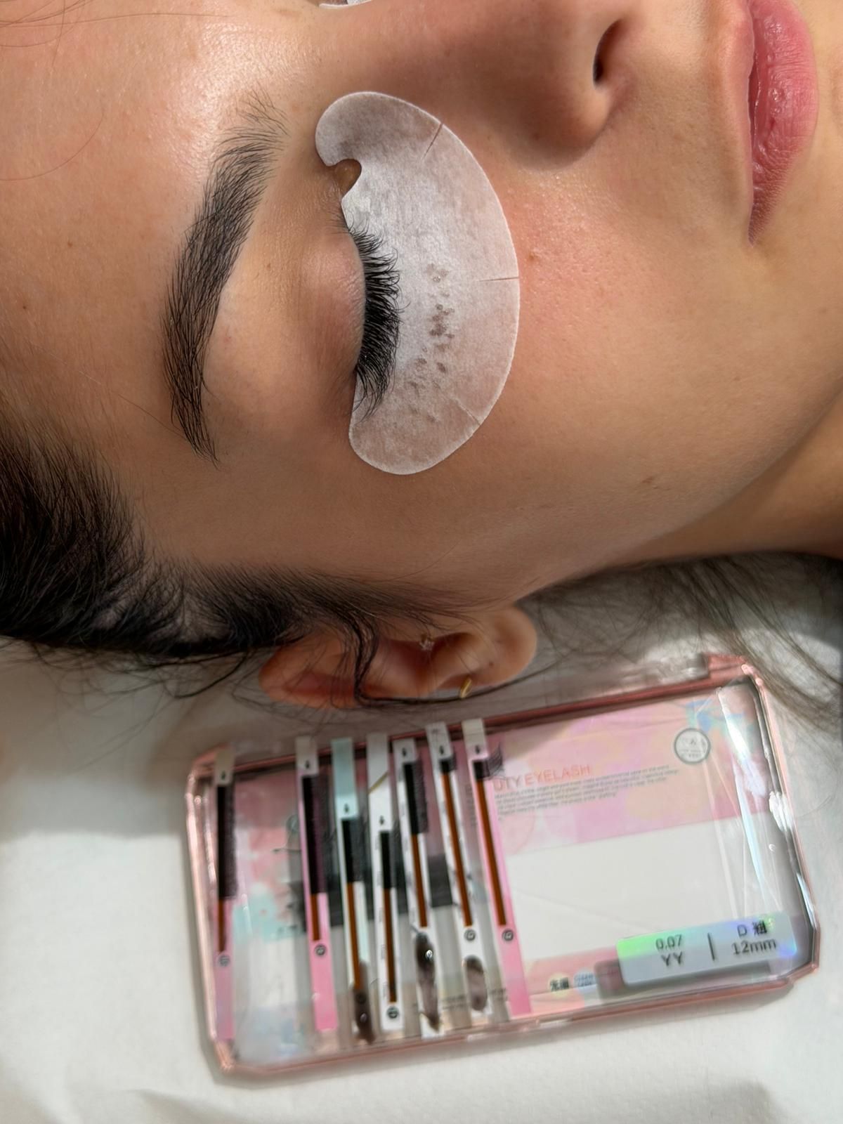 Primo piano di un viso addormentato con un cerotto bianco sotto gli occhi e un kit per il trucco rosa accanto.