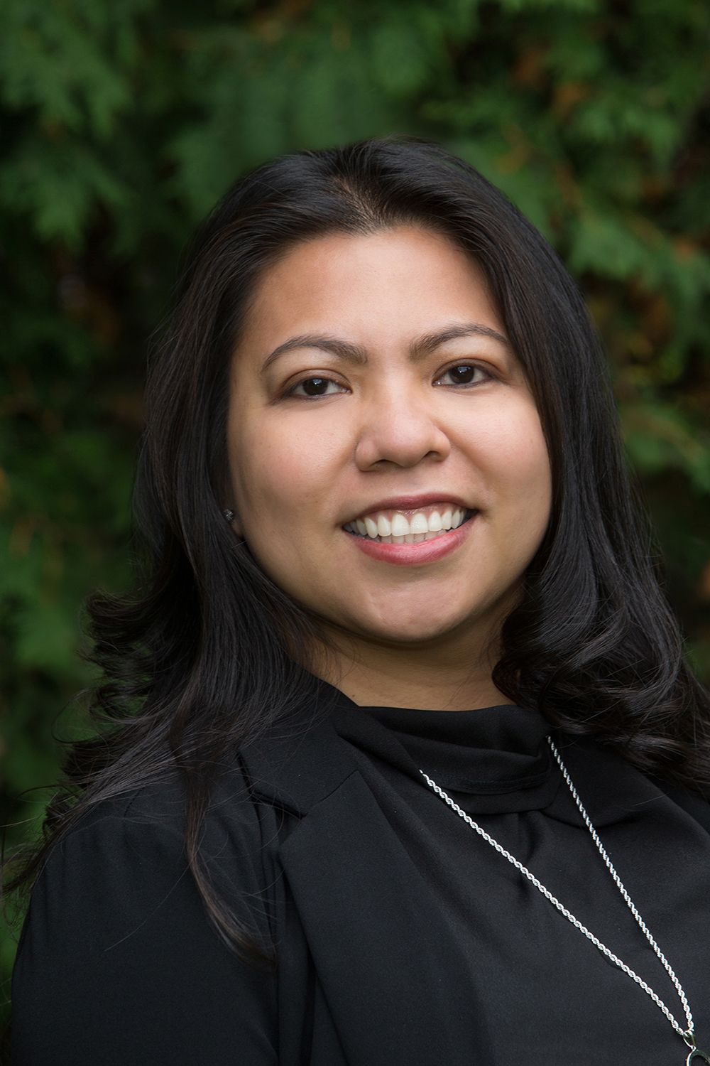 Woman smiling, wearing black blazer, against green background.