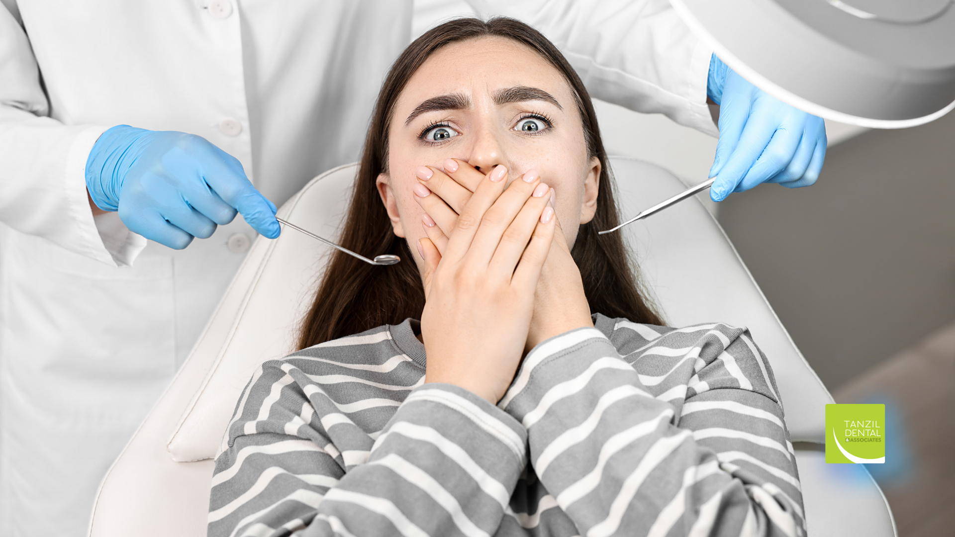 Person in a dental chair covering their mouth while gloved dentists prepare to examine them