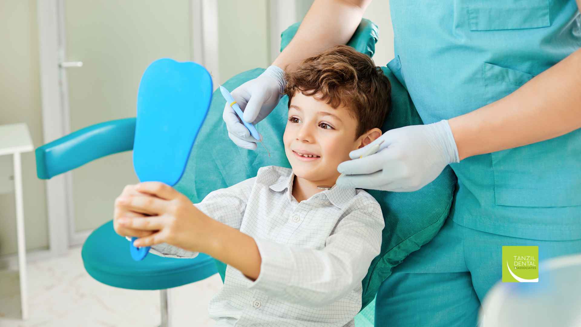 A young boy is sitting in a dental chair looking at his teeth in a mirror.