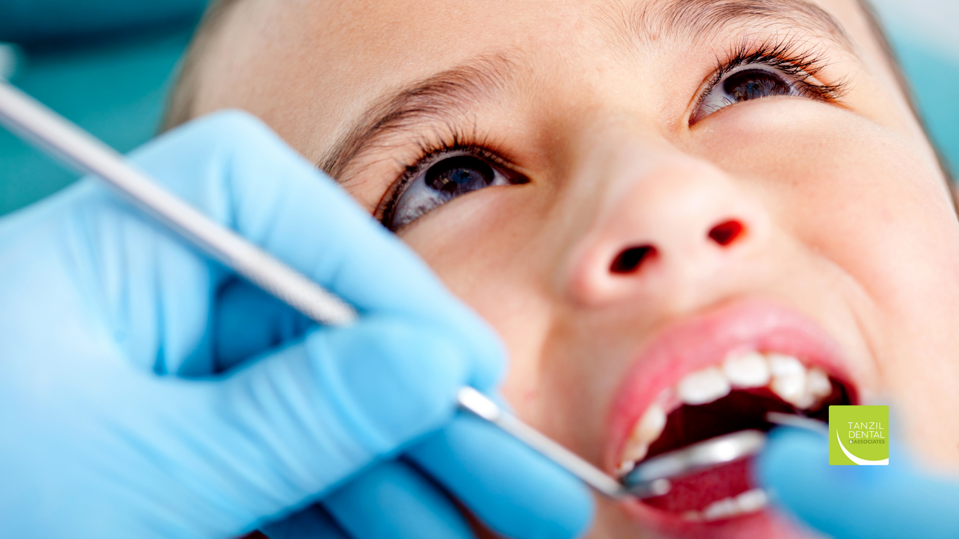 A young girl is getting her teeth examined by a dentist.