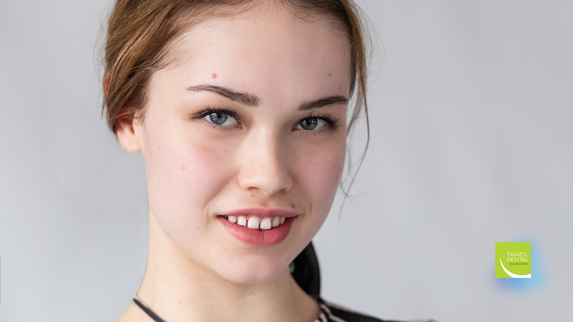 Woman with light skin, looking at the viewer with a slight smile. Light background.