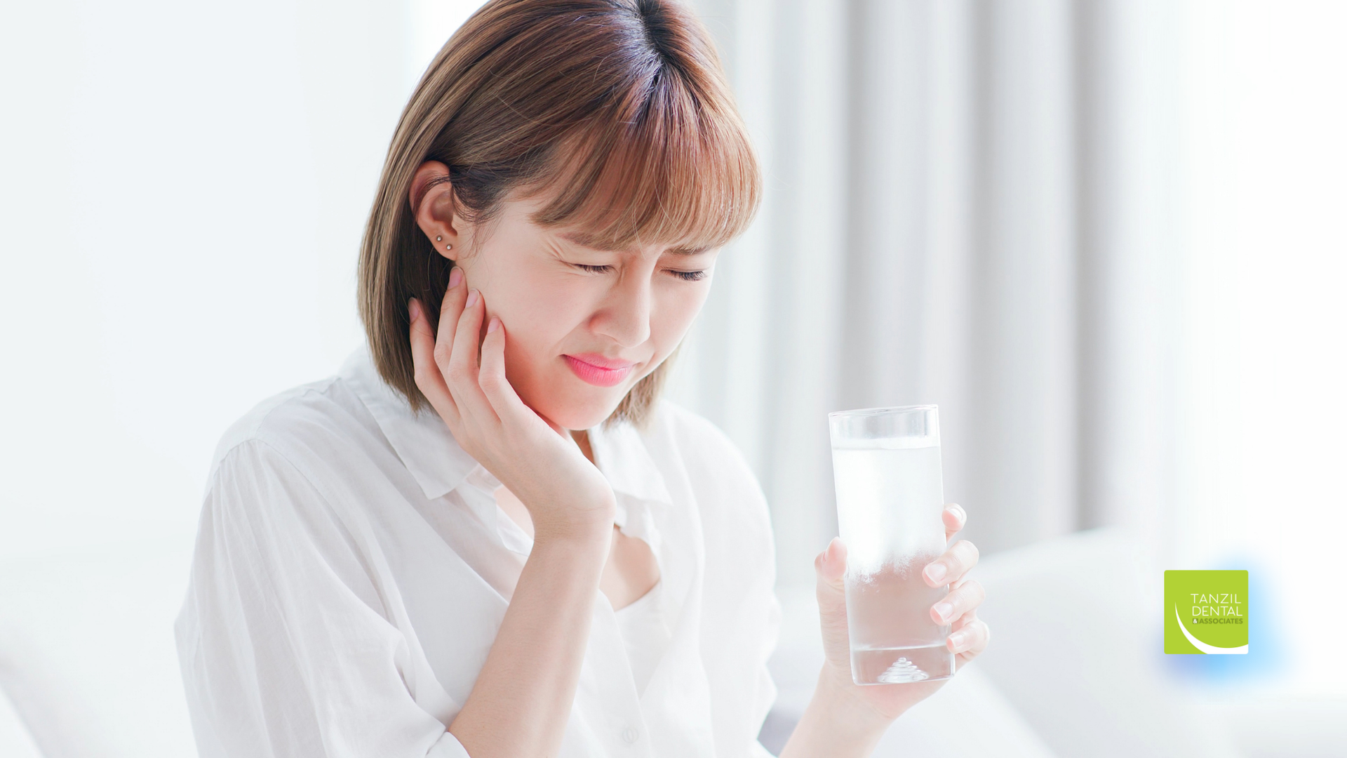 A woman is holding a glass of water and having a toothache.