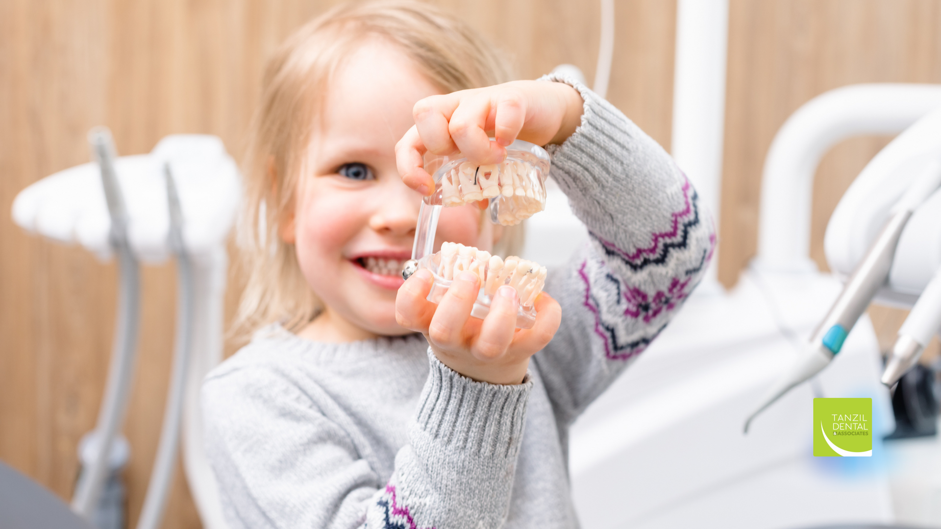 A little girl is holding a clear retainer in her hands in a dental office.