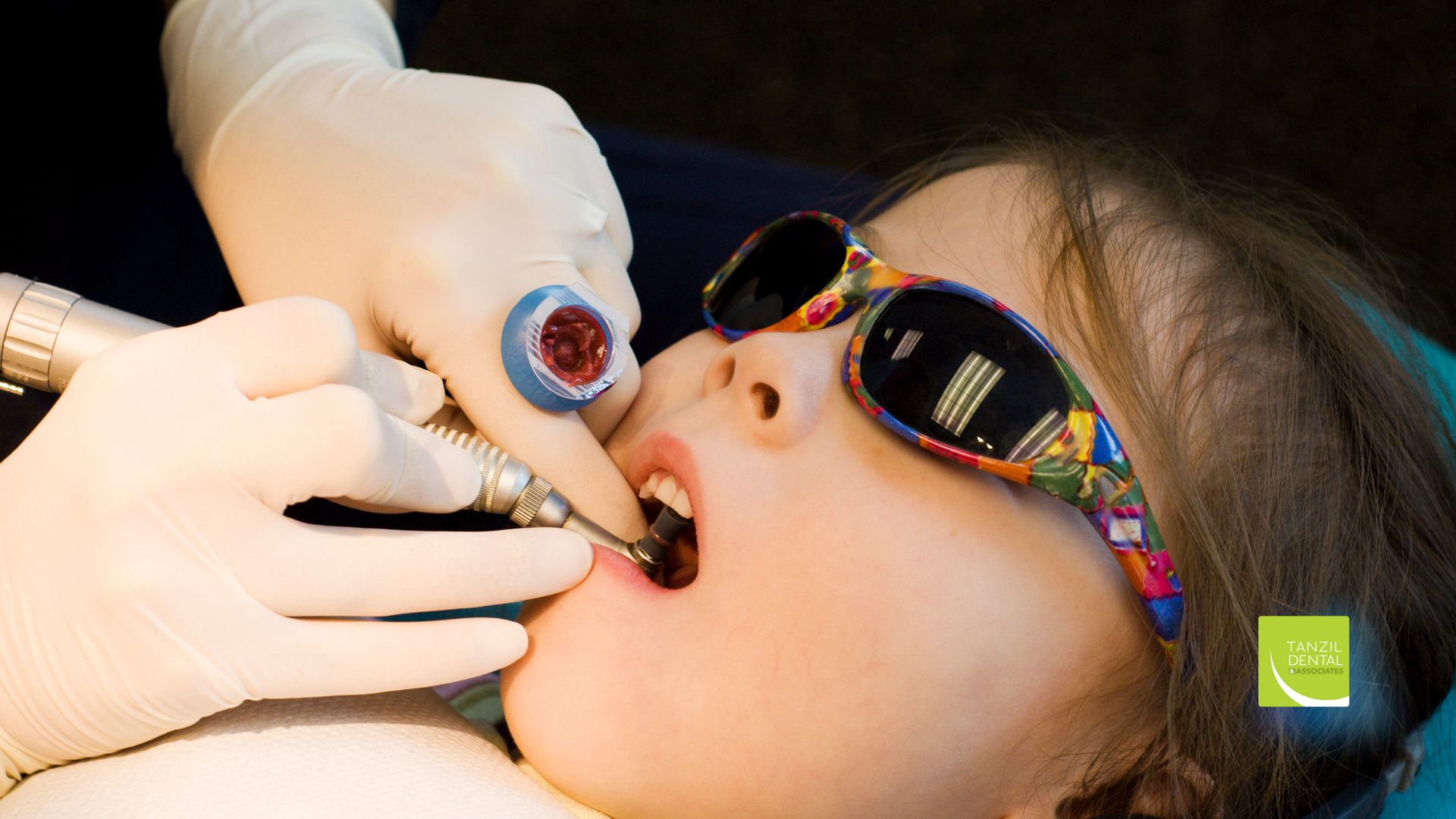 A young girl wearing sunglasses is getting her teeth examined by a dentist.