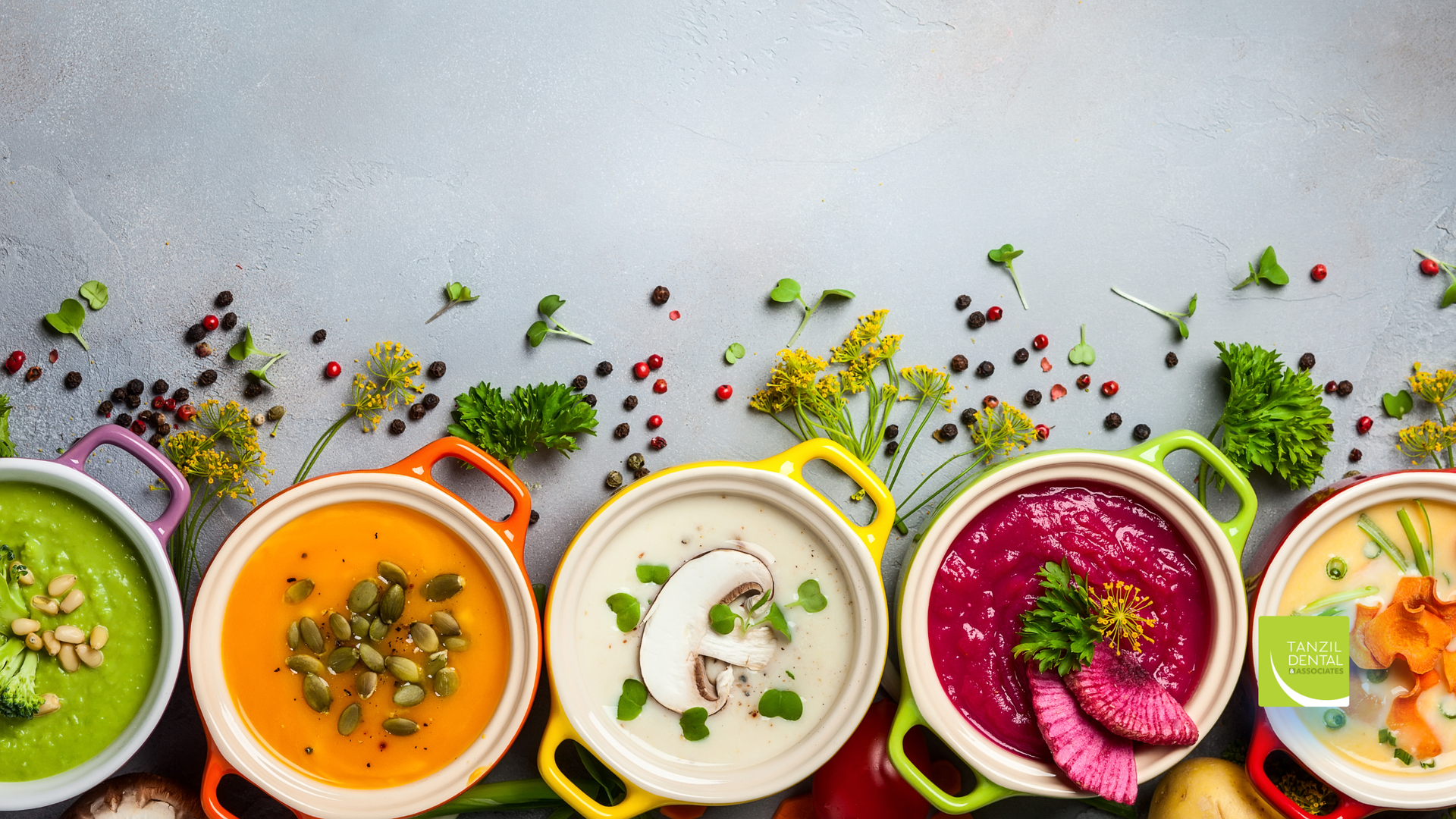 Colorful bowls of soup arranged on a gray surface, garnished with herbs and spices.
