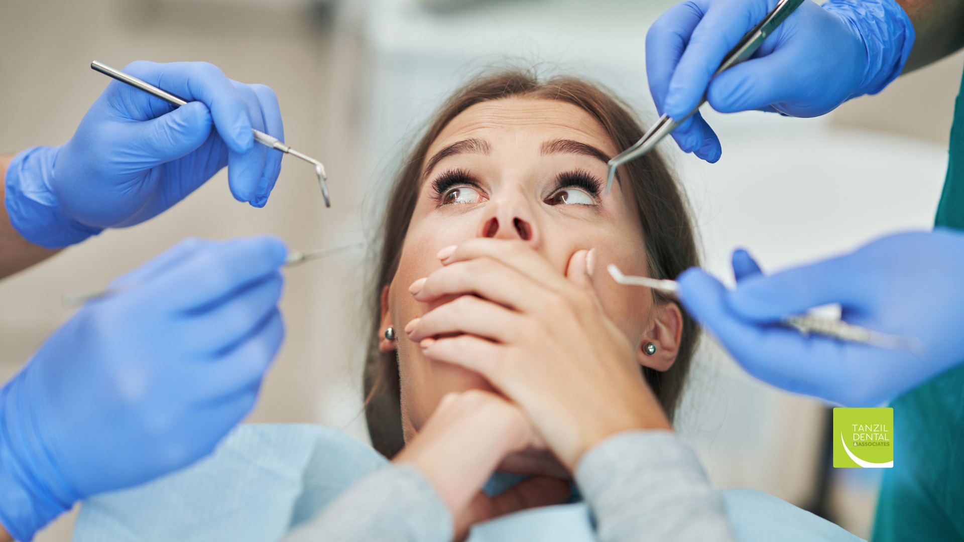 Woman in dental chair, fearful, with hands covering mouth, surrounded by dentists with tools.