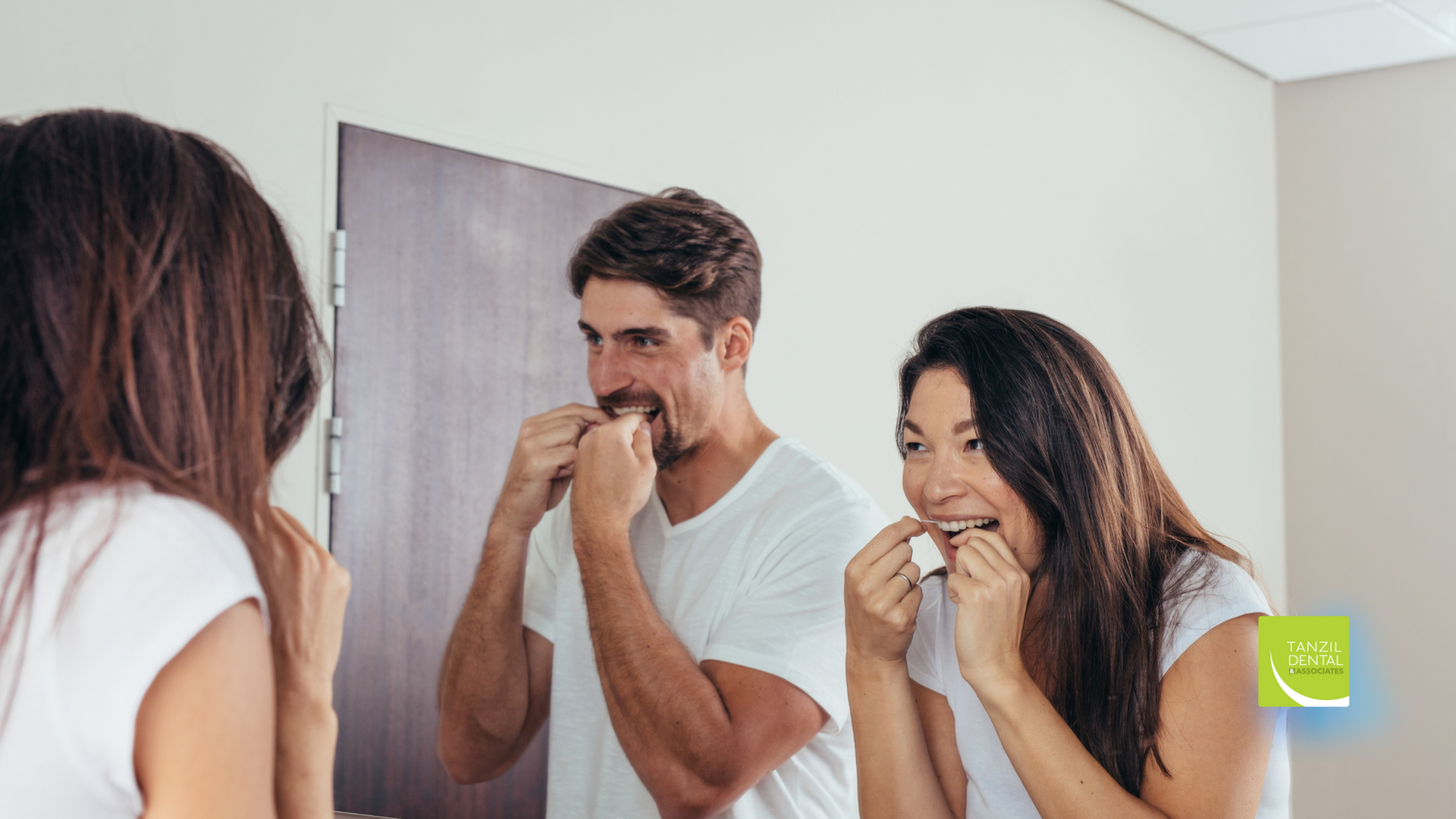 Three people flossing their teeth in front of a mirror in a bathroom.