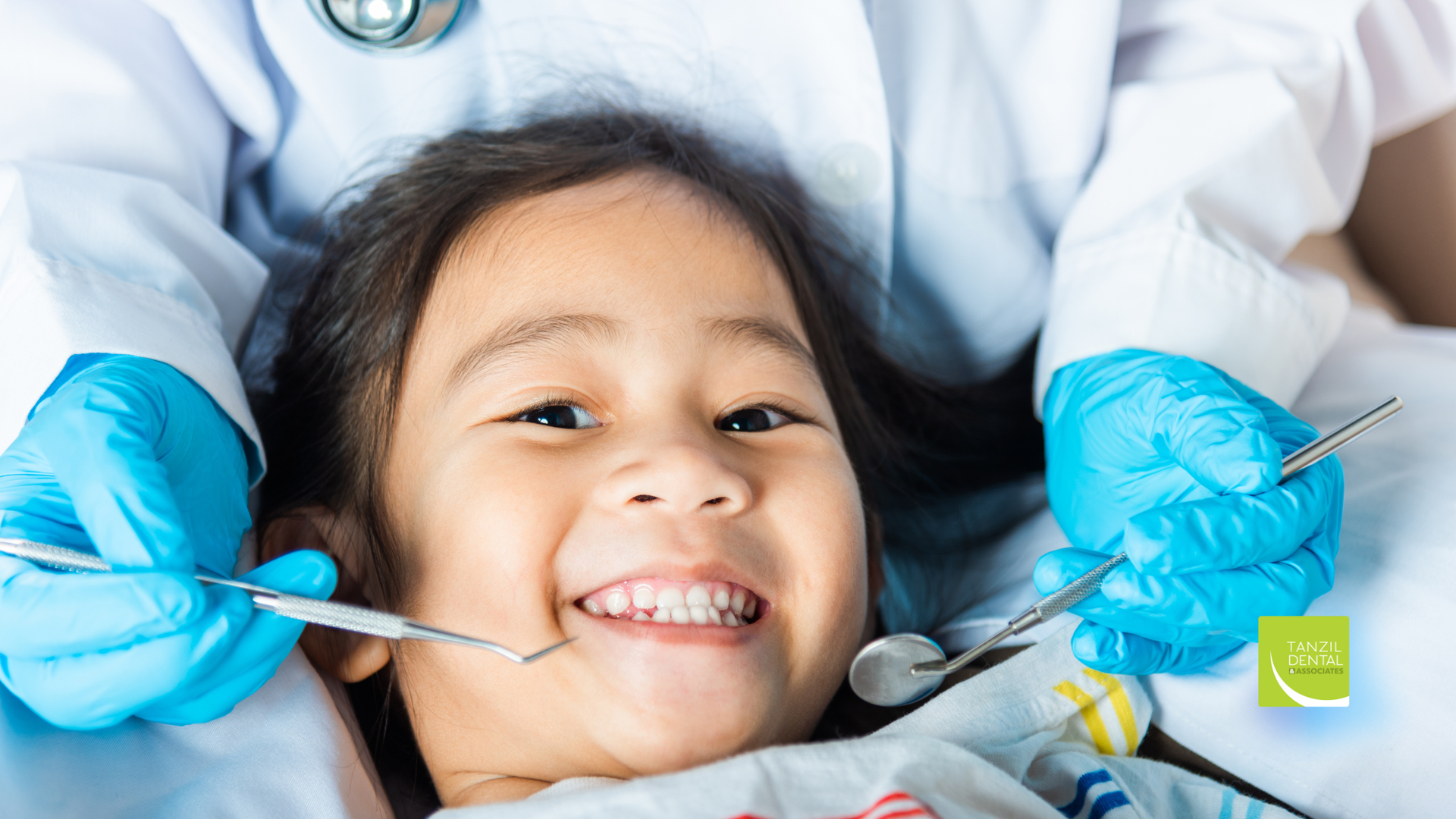 Young patient smiling during a dental exam. Dentist in blue gloves holds tools.