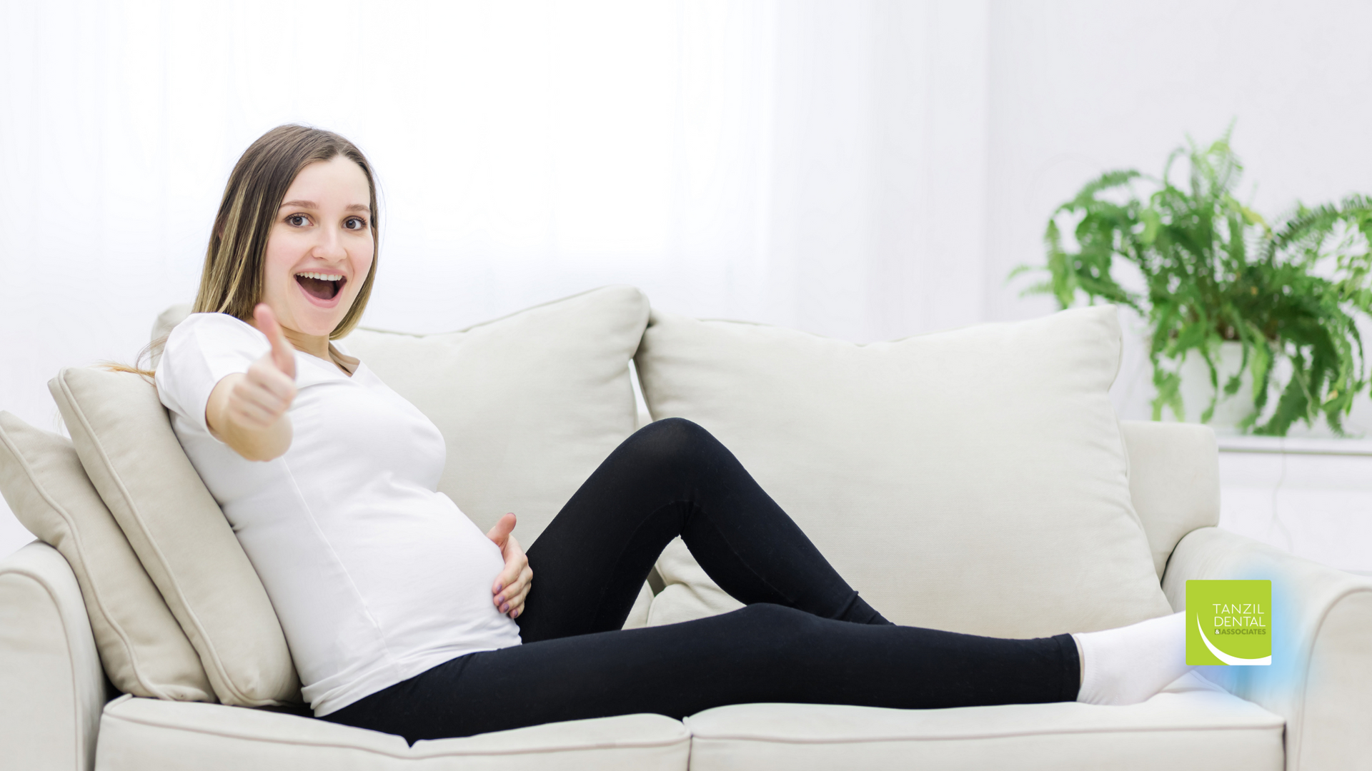 A pregnant woman is sitting on a couch and giving a thumbs up.