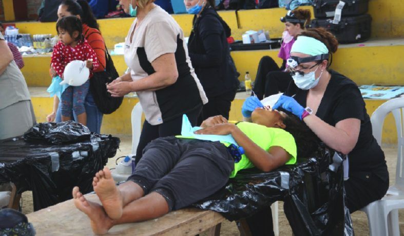 Dentist treating a person outdoors; others wait and observe.