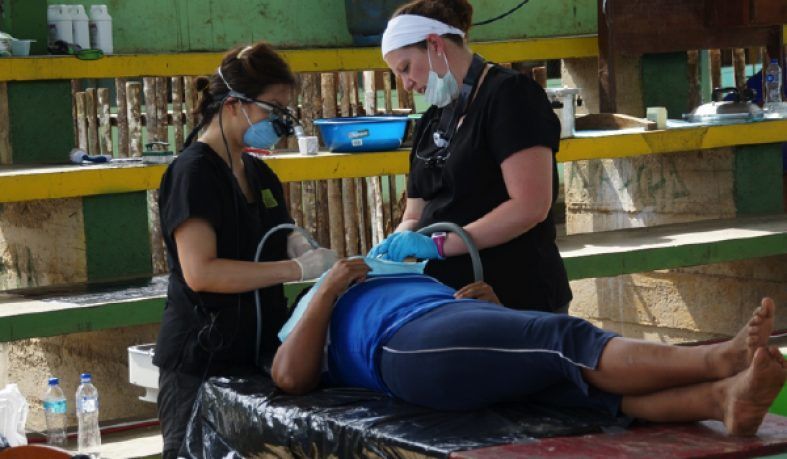 Two dental professionals provide care to a patient lying down on a table outdoors.