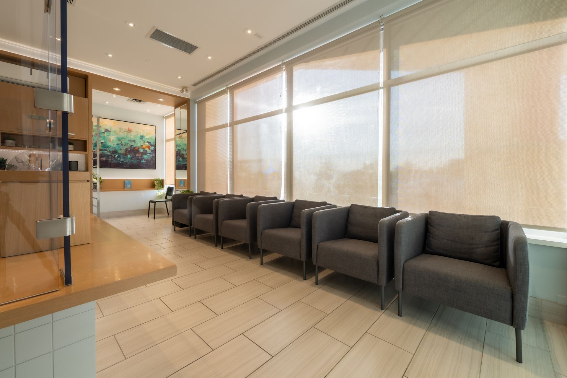 Waiting room with gray chairs, large windows with shades, and neutral-colored walls and floor.