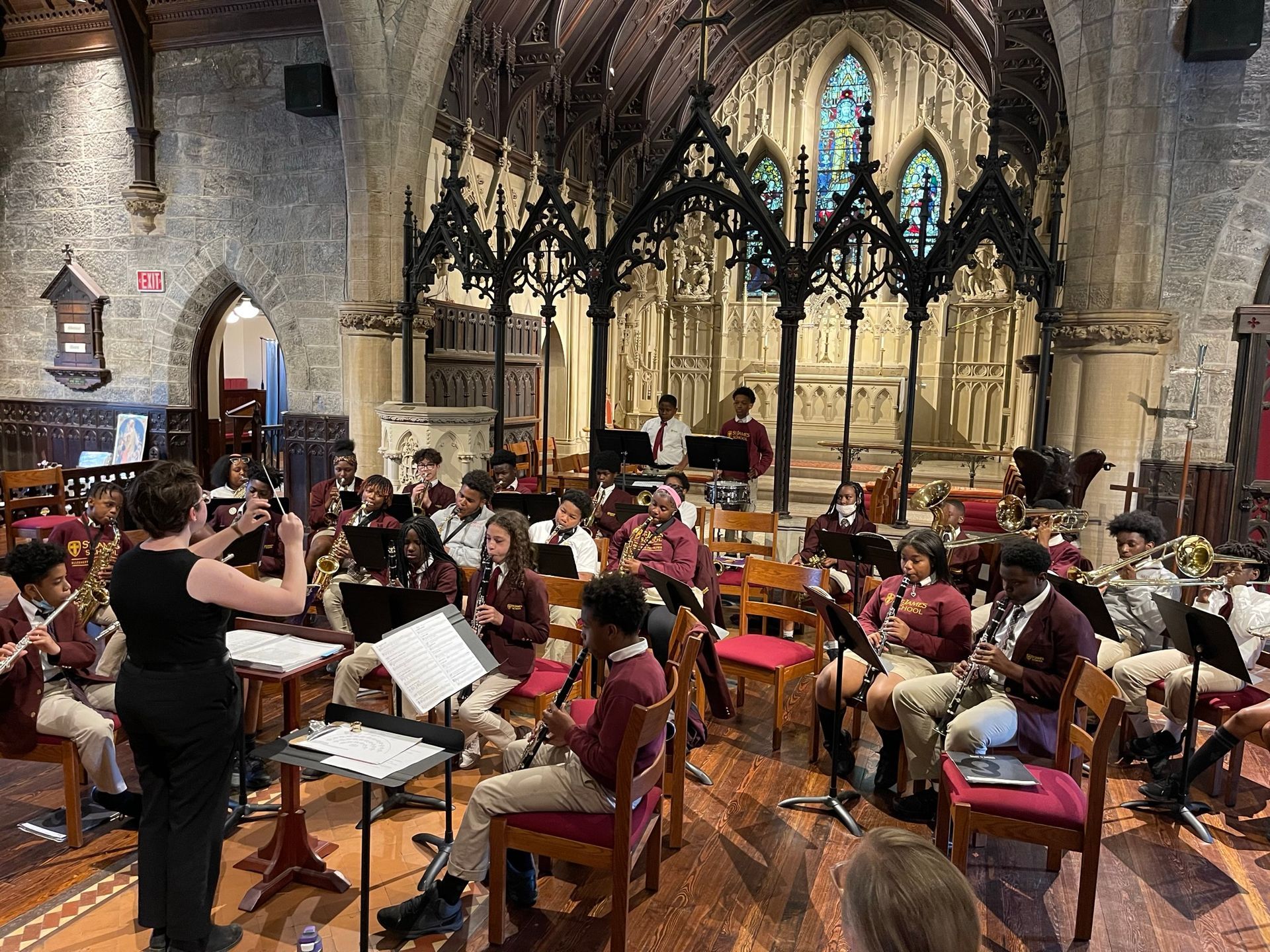 A conductor leads a student orchestra performing on musical instruments inside a historic stone church.