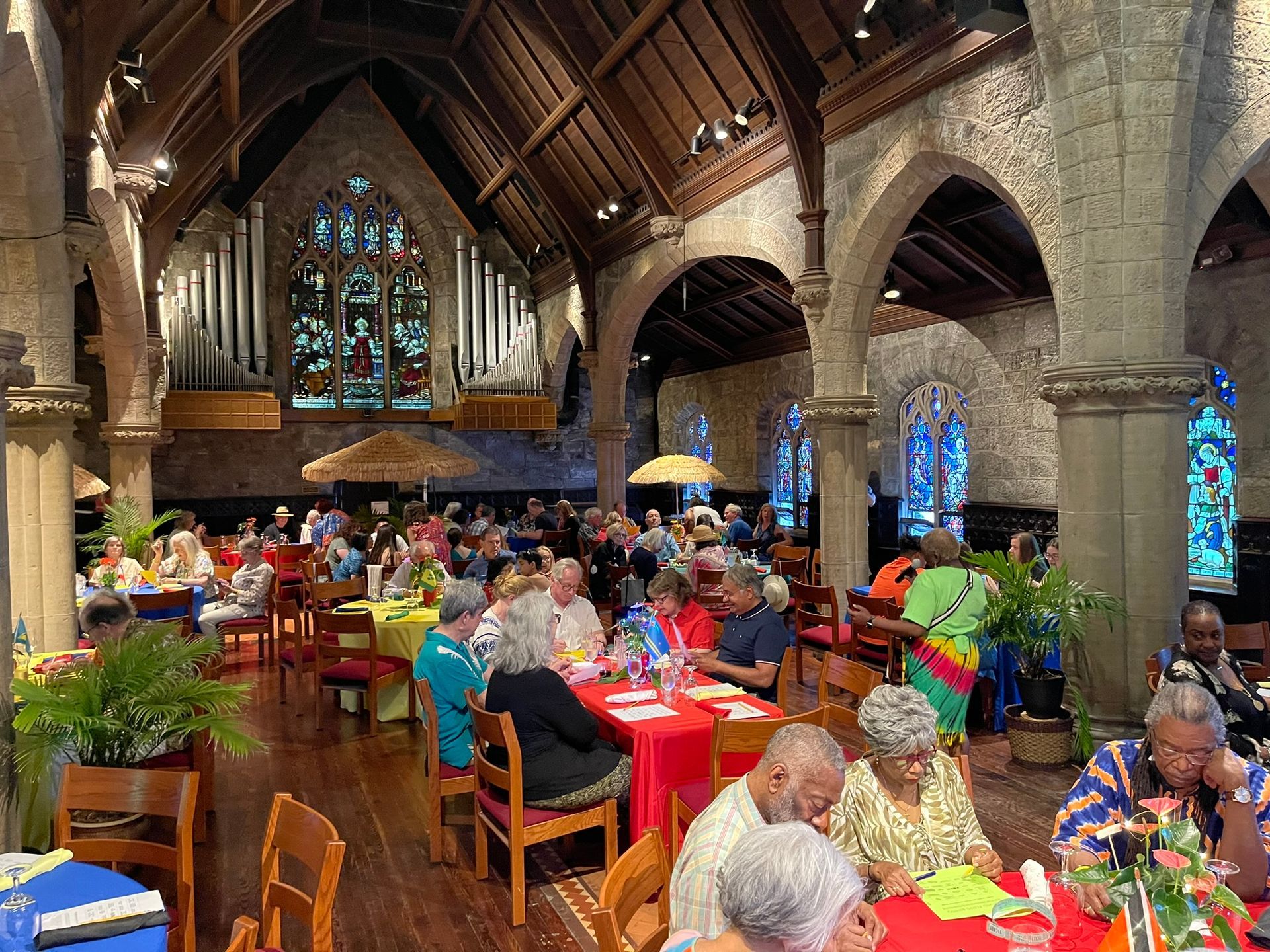 A group gathers for a meal inside a historic stone church featuring vaulted ceilings, wooden beams, and stained glass.