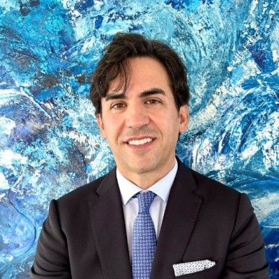 Man in a dark suit smiling in front of a blue abstract painting background