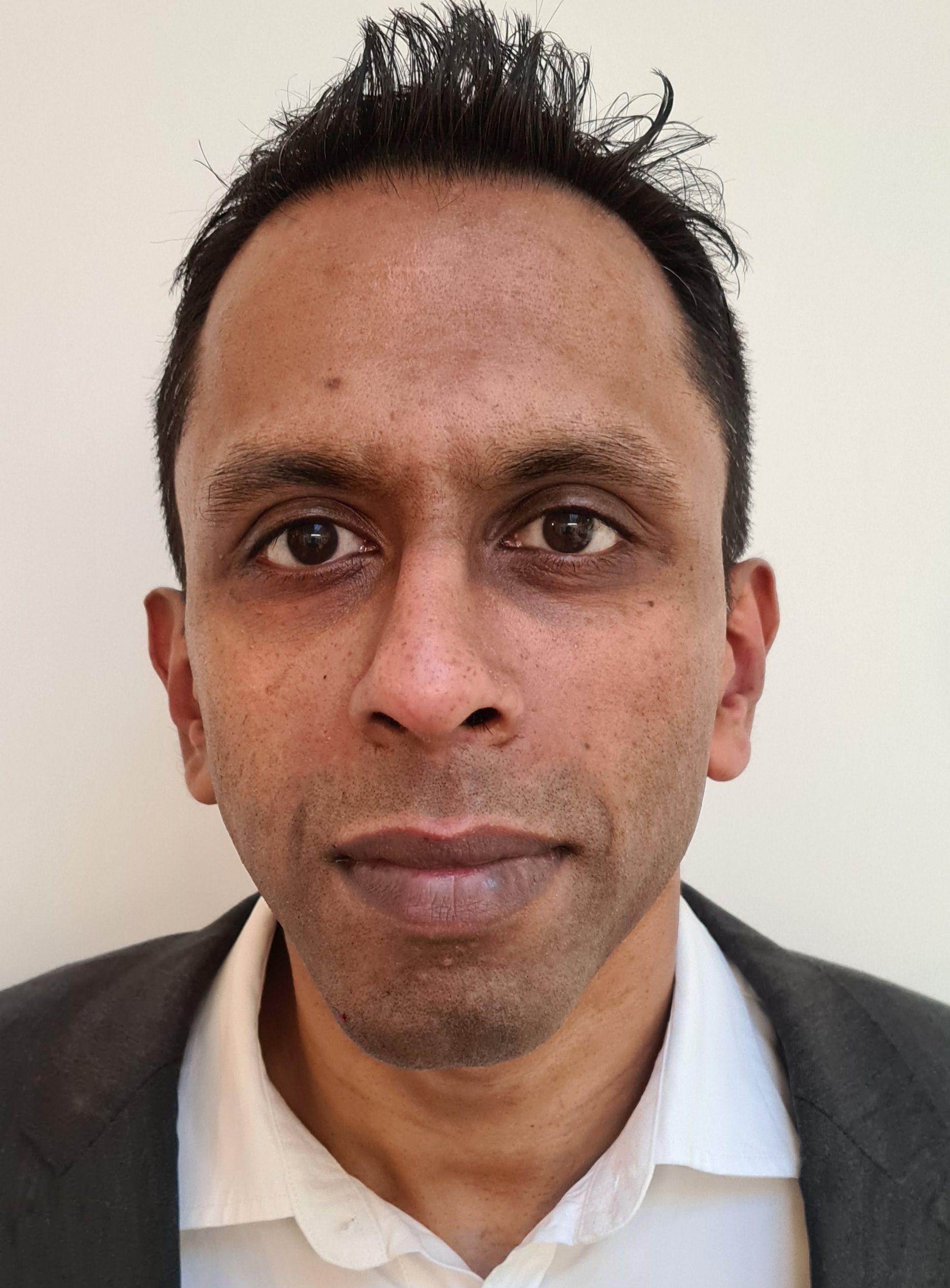 Portrait of a man in a dark jacket and white shirt against a plain light background