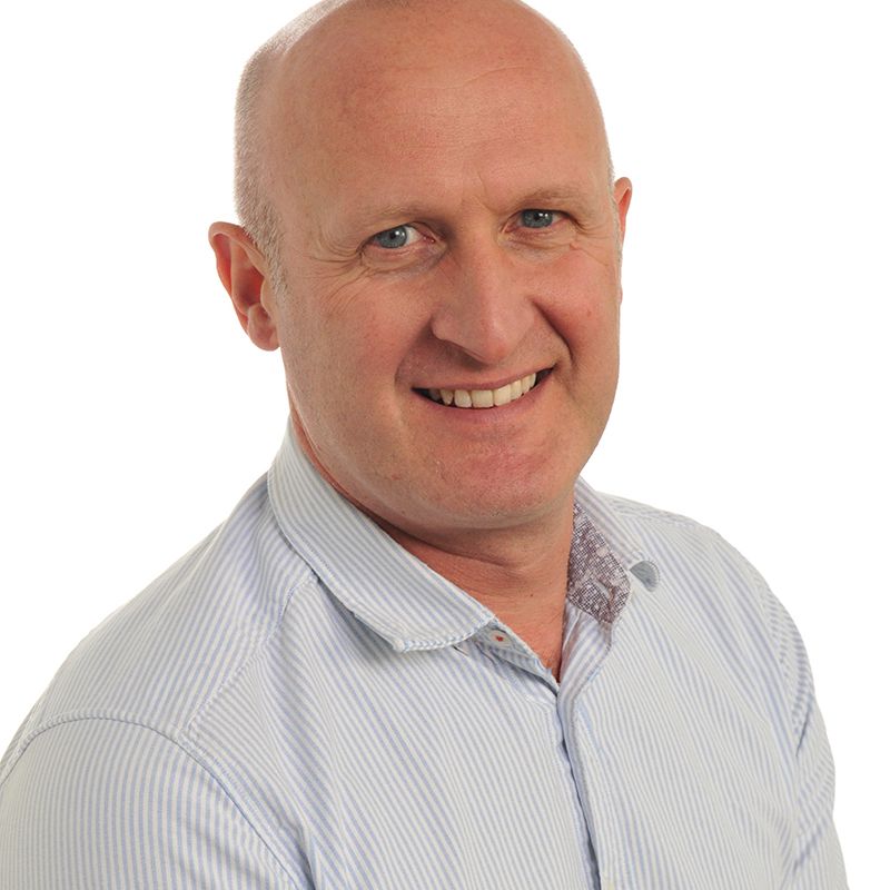 Smiling bald man in a light blue striped shirt against a white background