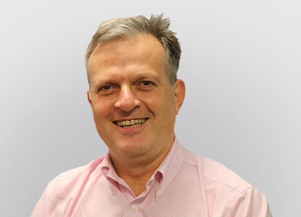 Smiling man in a pink shirt against a plain light gray background