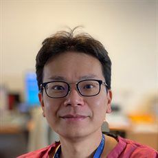 Person wearing glasses and a red shirt, smiling in a softly blurred indoor setting.