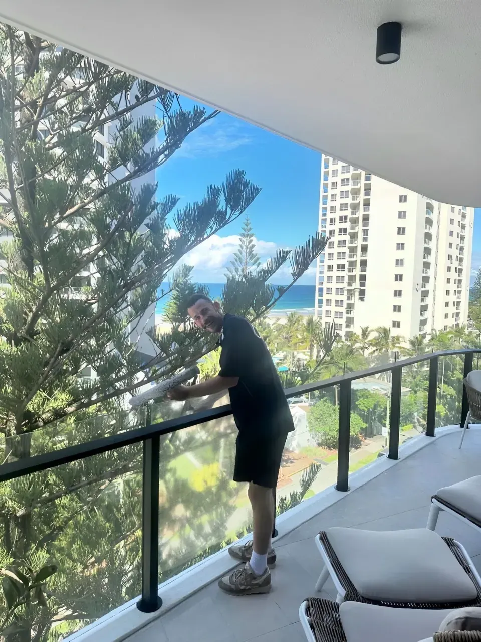 A Man Is Standing On A Balcony Cleaning The Glass — Supercare Gold Coast In Broadbeach, QLD