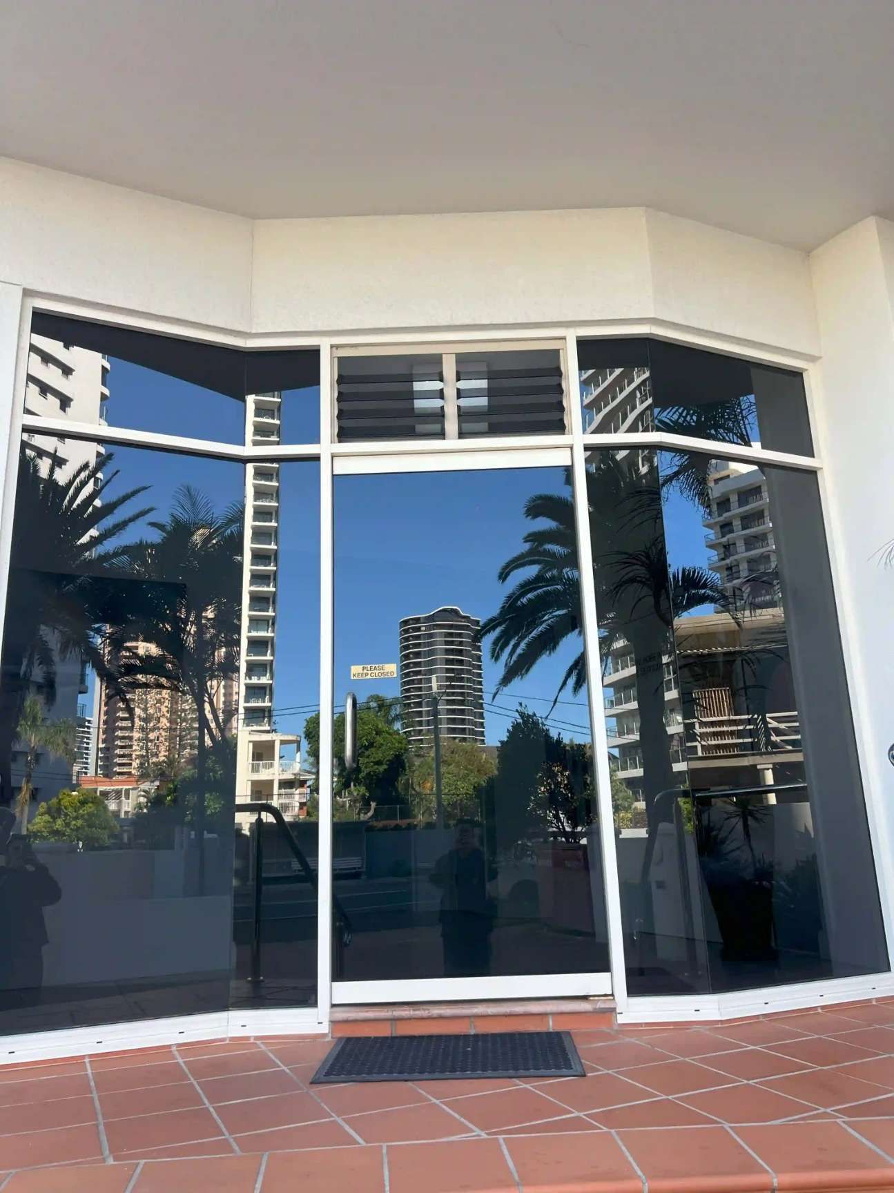 A Large Glass Door With A Reflection Of Palm Trees And Buildings In It — Supercare Gold Coast In Miami, QLD