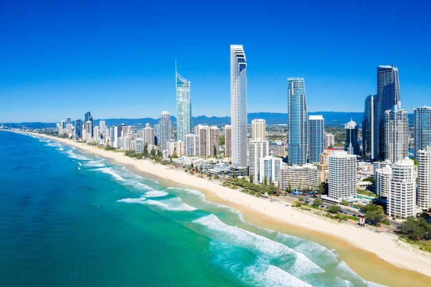 Aerial View of a City With a Beach and a City SkylineTree Branch is Laying on a Sandy Beach With a Sailboat in the Distance — Supercare Gold Coast in Broadbeach, QLD