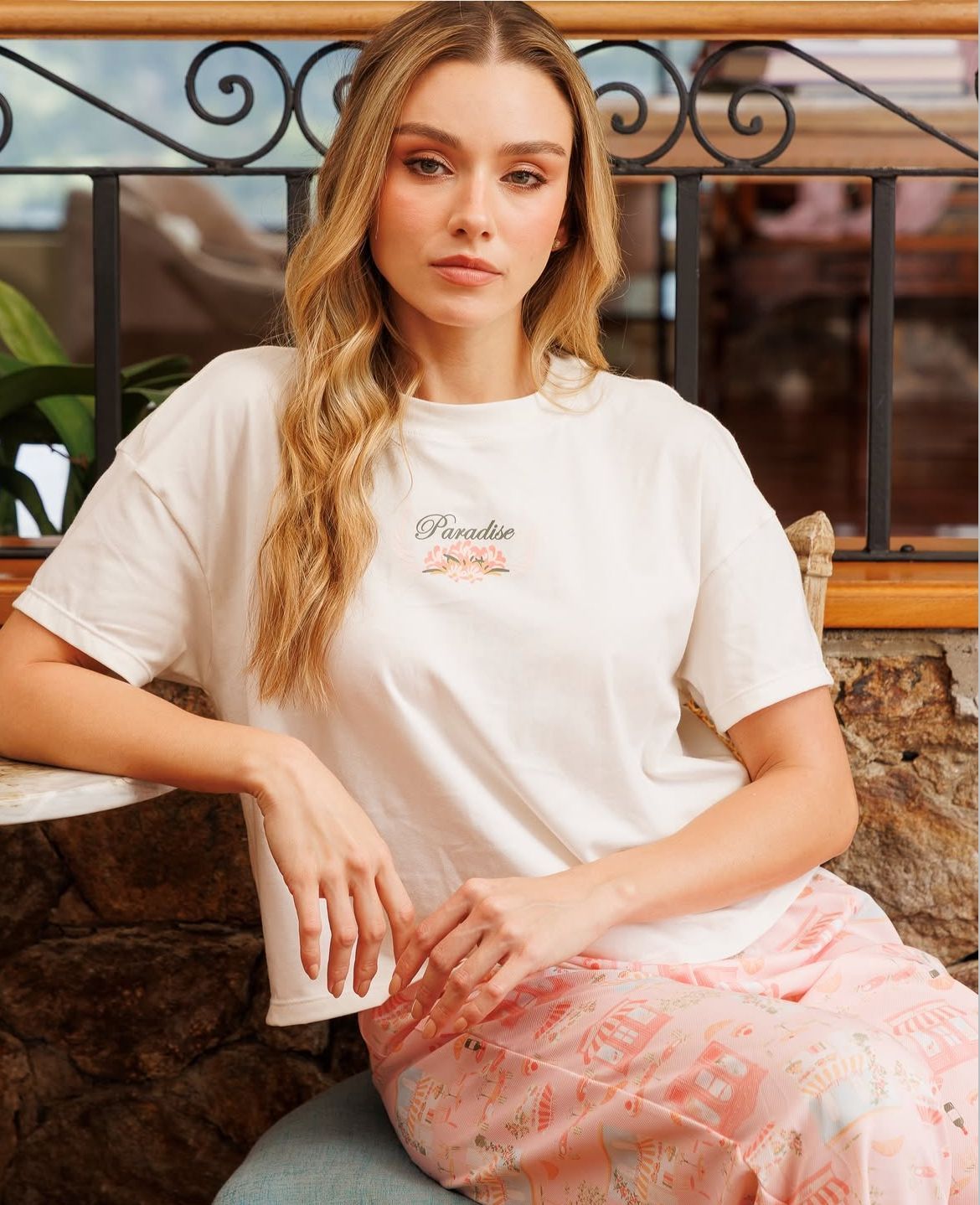 Mujer sentada en unos escalones, con camiseta blanca y falda rosa, mirando a la cámara.