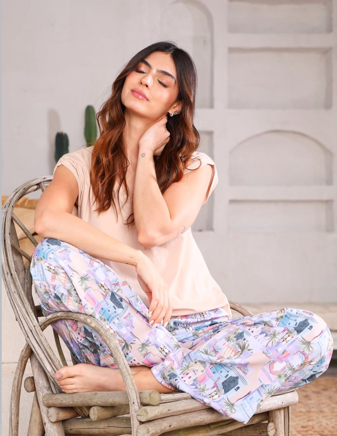 Mujer sentada en una silla de mimbre, con los ojos cerrados, vestida con una blusa clara.