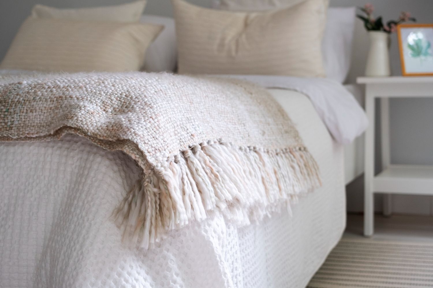 Acogedora habitación con una manta texturizada de color beige sobre una cama blanca, junto a una pequeña mesita de noche.