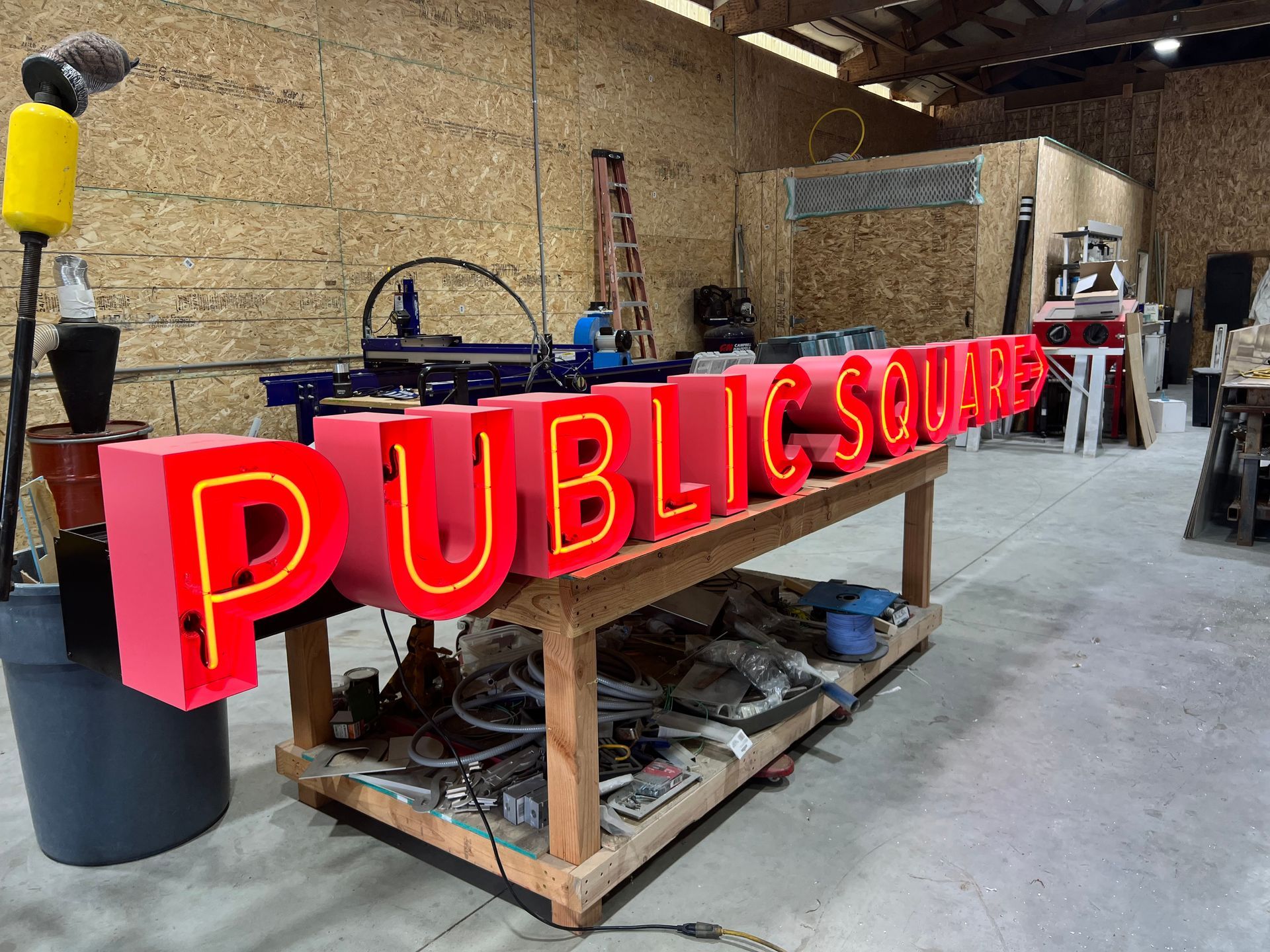 Pink sign with yellow neon on a wooden workbench in a workshop