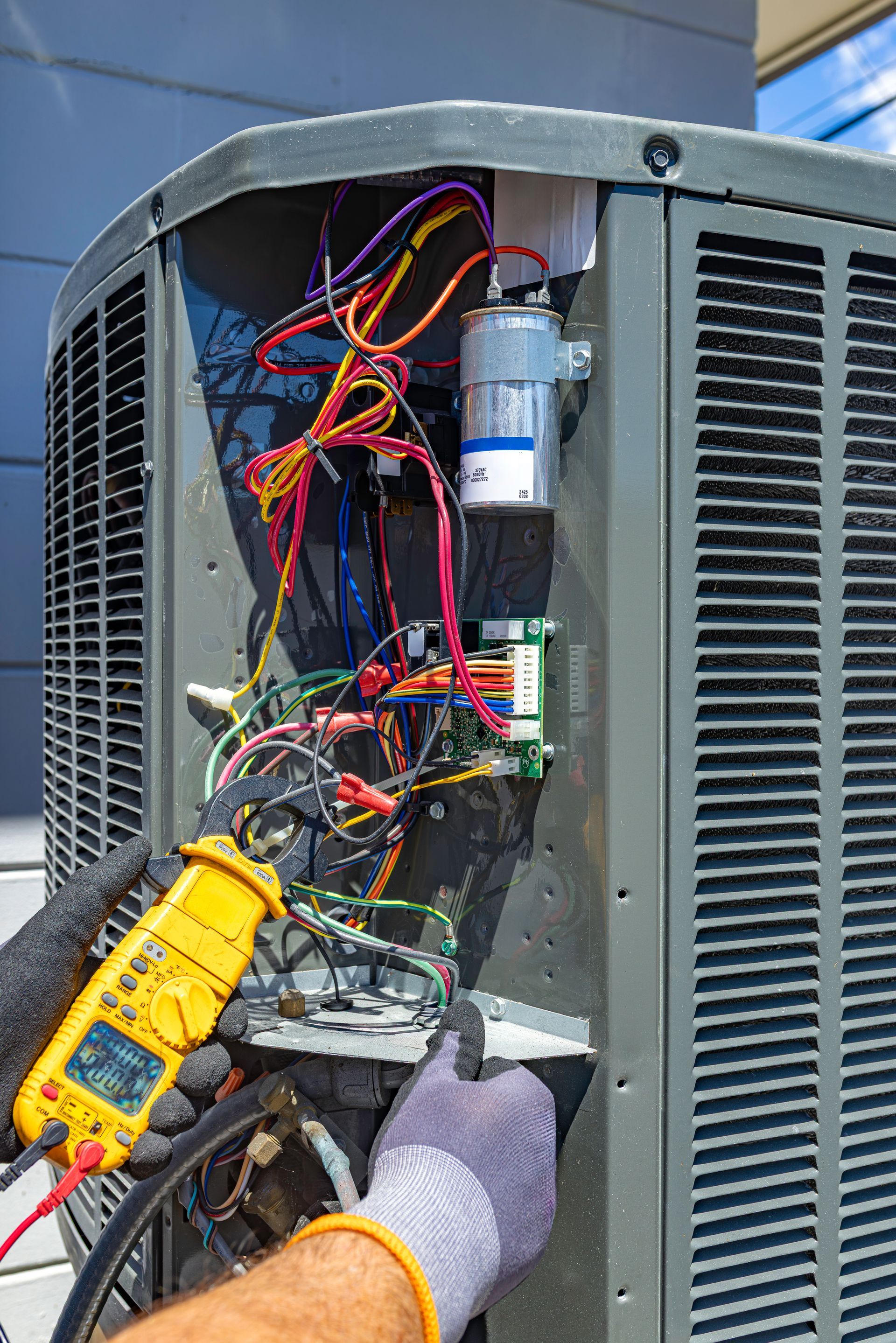 Technician testing exposed electrical wiring in an outdoor utility cabinet with a multimeter