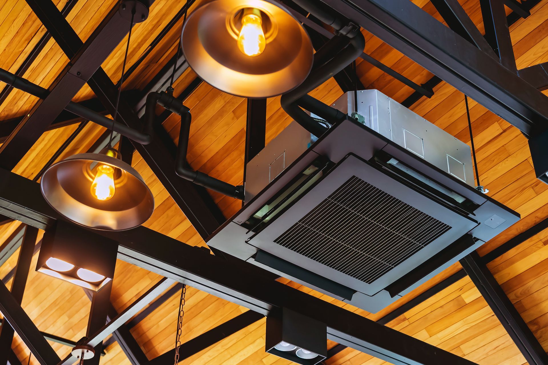 Ceiling with warm lights and a square air vent among dark beams and wooden panels
