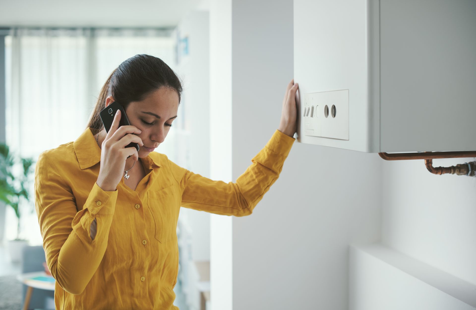 Woman in a yellow shirt talking on a phone beside a wall-mounted electrical panel