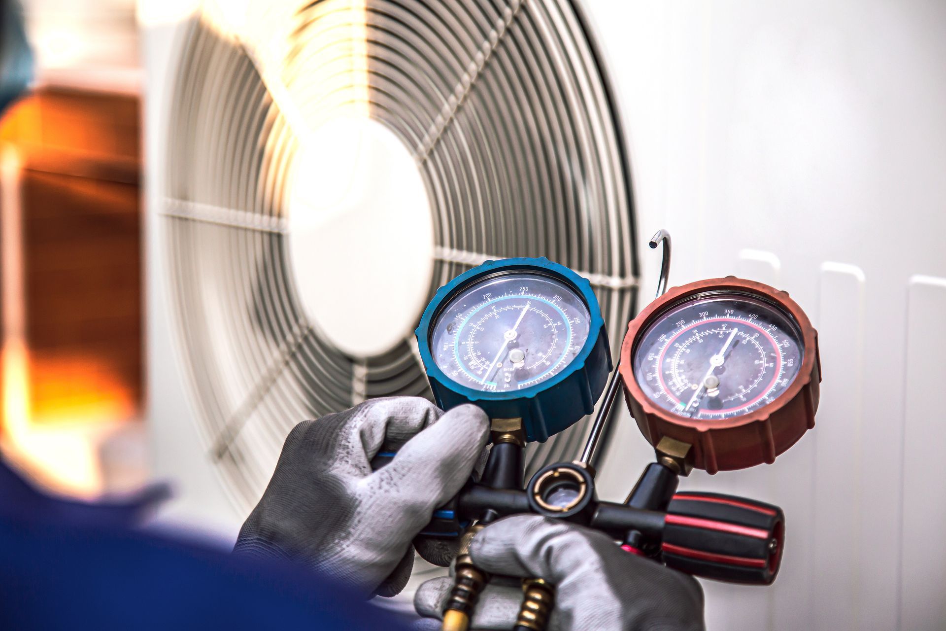 Gloved hands holding HVAC gauges beside an outdoor air conditioner unit