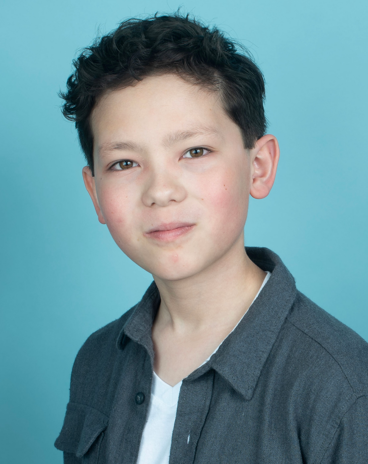 A young boy with curly hair is wearing a gray shirt and a white shirt.