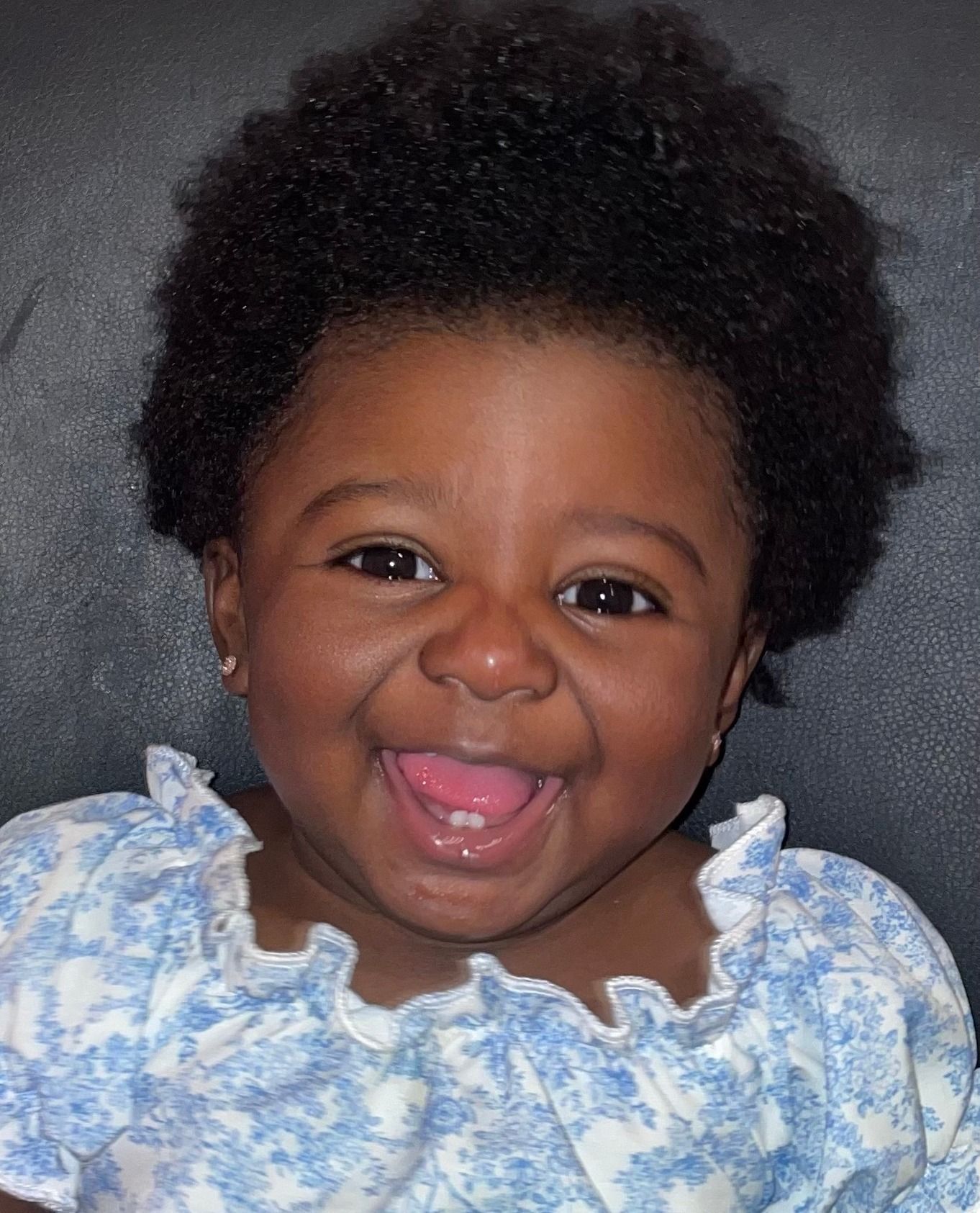 A baby in a blue and white dress is smiling with her tongue out