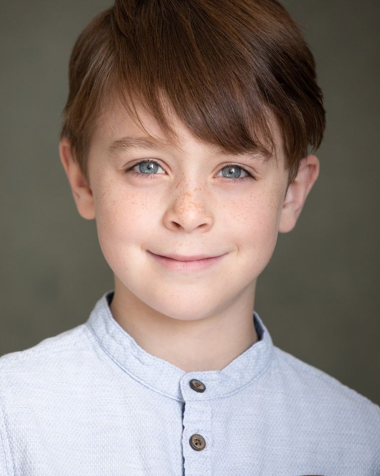 A young boy with brown hair and blue eyes is smiling for the camera.