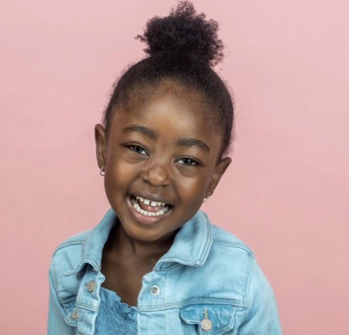 A little girl is wearing a denim jacket and smiling.