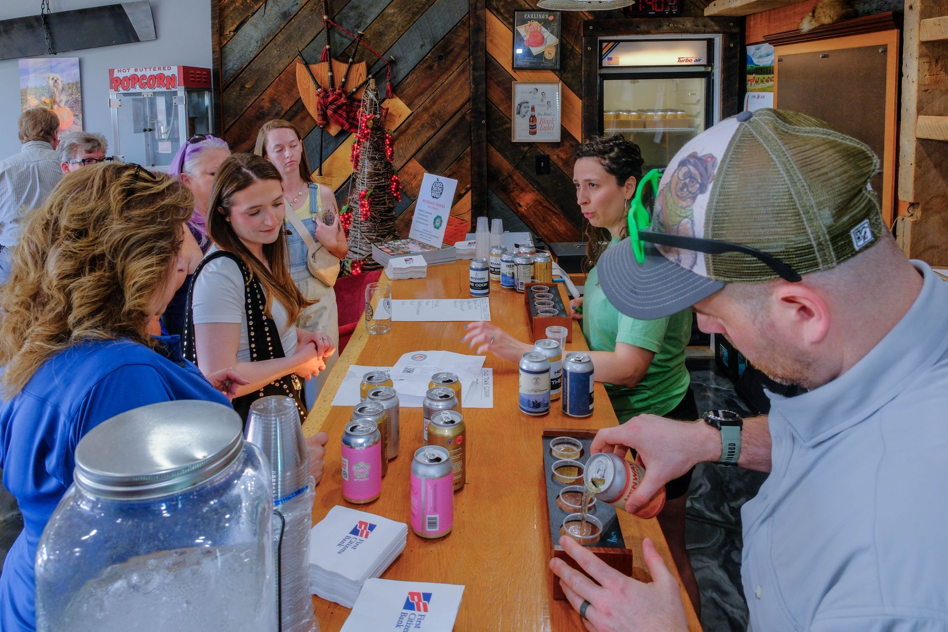 People seated at a long table in a cozy bar, eating, drinking, and chatting around a Christmas tree.