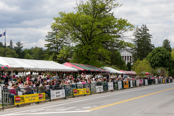 Crowd behind barricades at parade in corporate suites under white tents on a tree-lined street