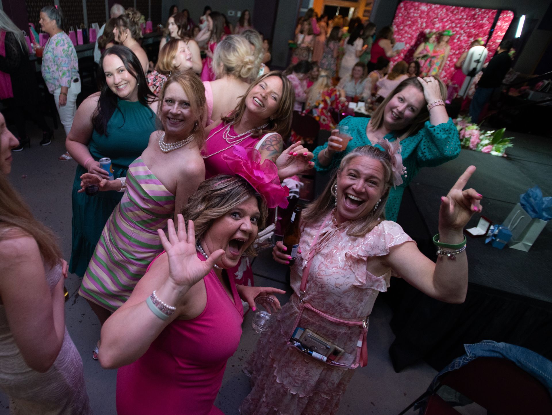 People dancing and posing at a lively party, wearing pink outfits and smiling on a crowded dance floor.