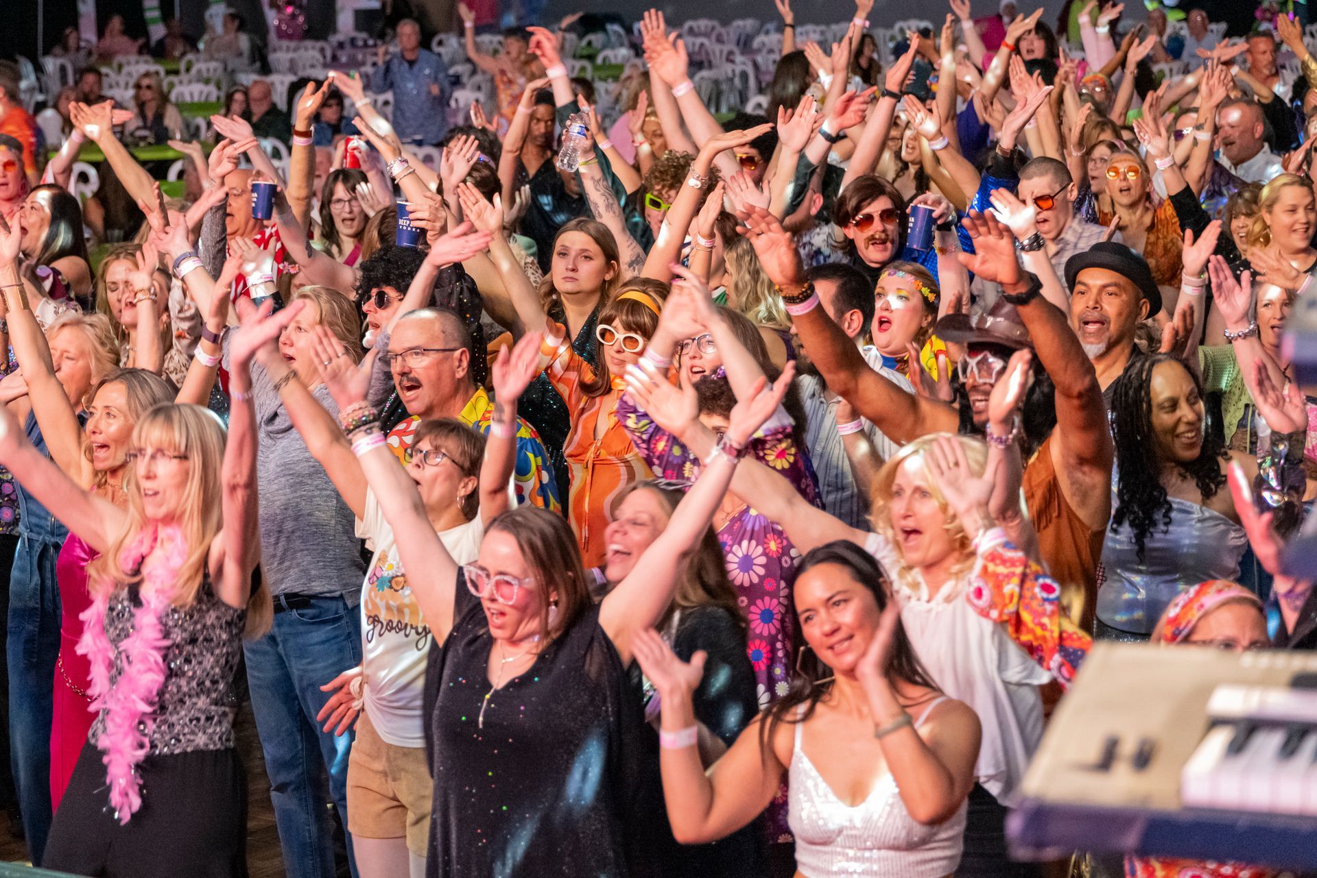 Crowd dancing and cheering at a concert, with raised hands and colorful festival outfits