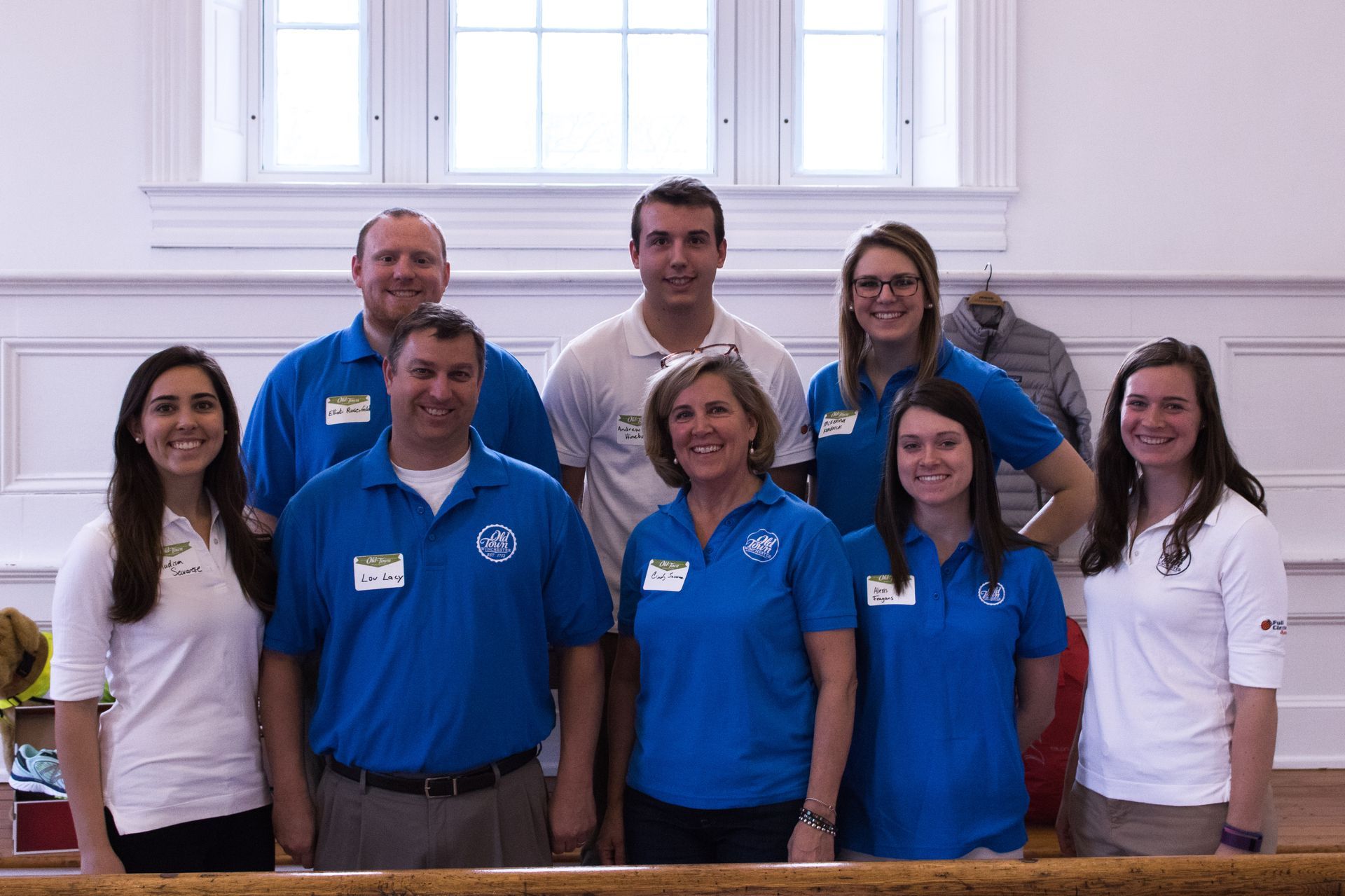 Group of smiling people in blue and white shirts posing indoors on church pews