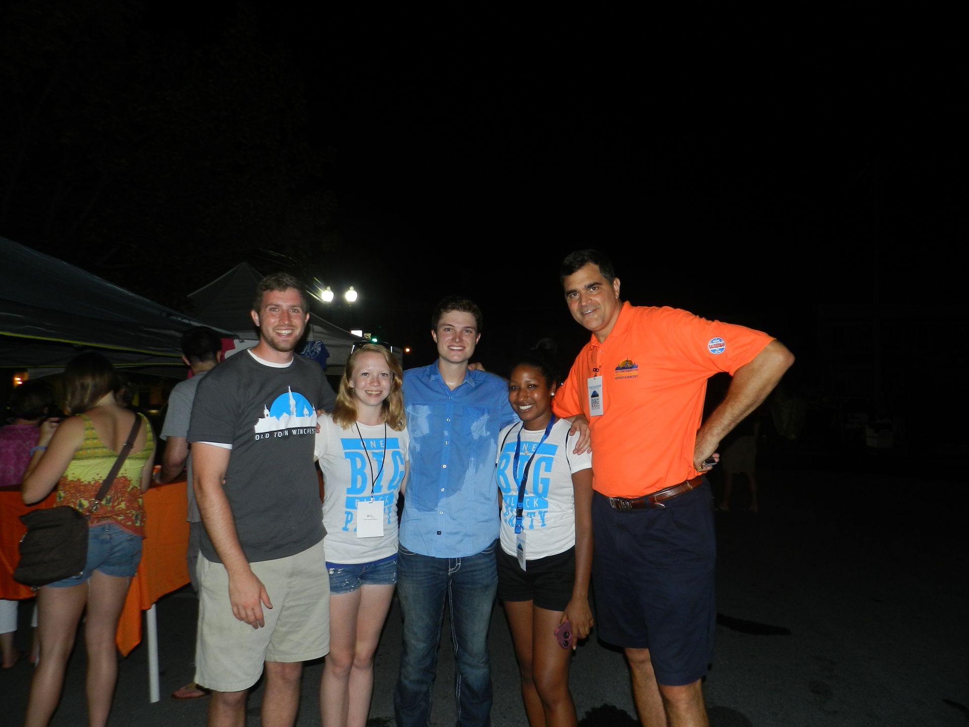 Four people posing outdoors at night, two wearing blue event shirts and one in an orange shirt.
