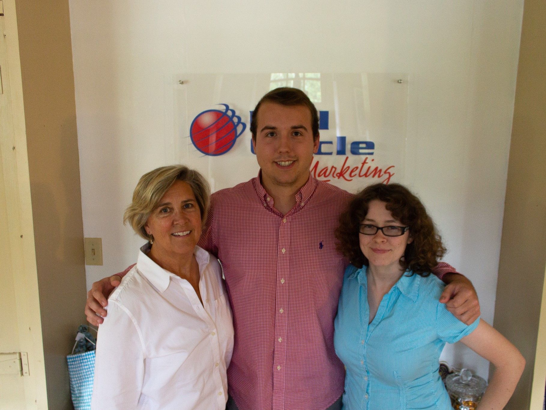 Three people posing indoors in front of a company logo, smiling at the camera.