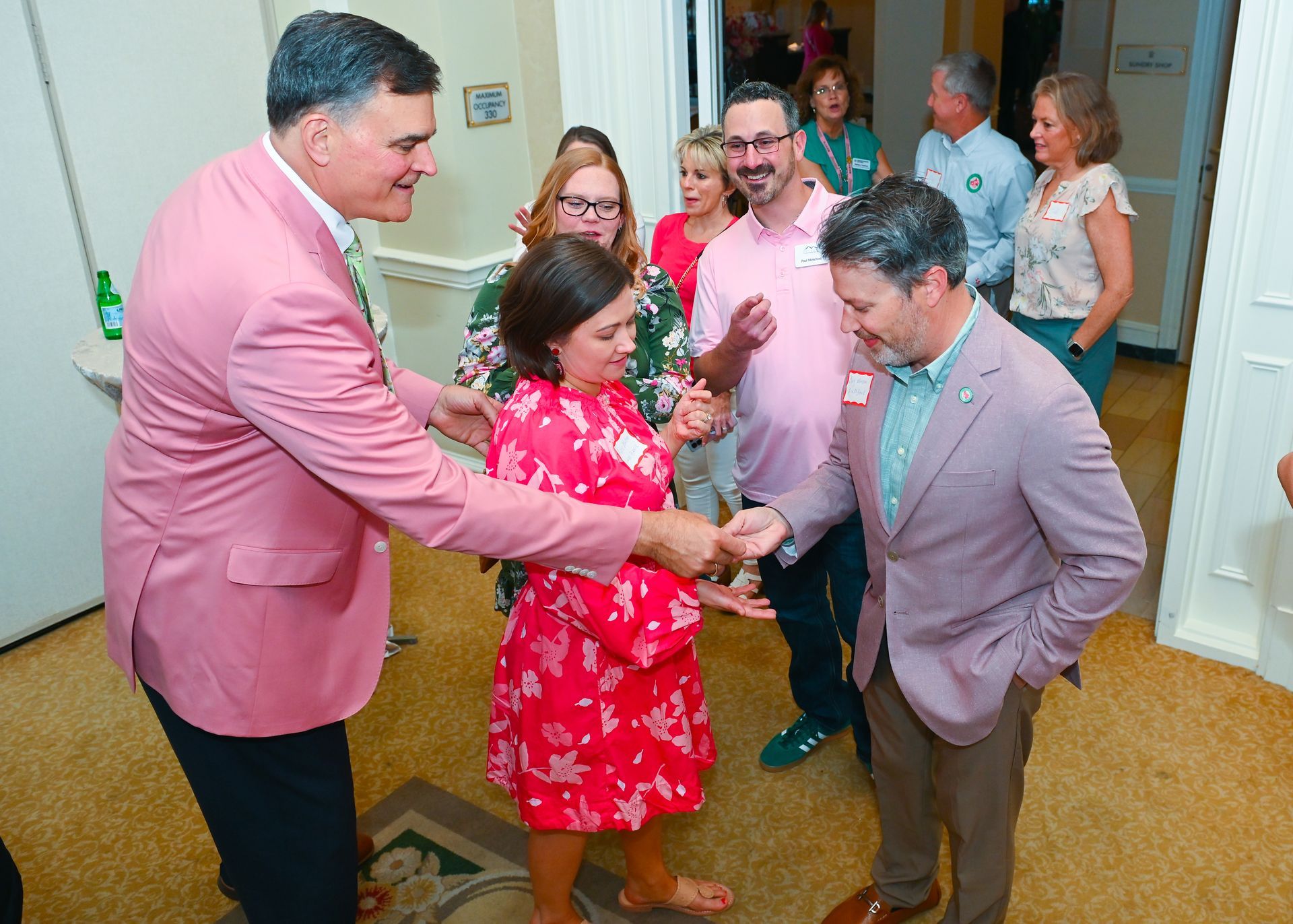 Three people in bright pink and green jackets posing together at a lively indoor event employee reward