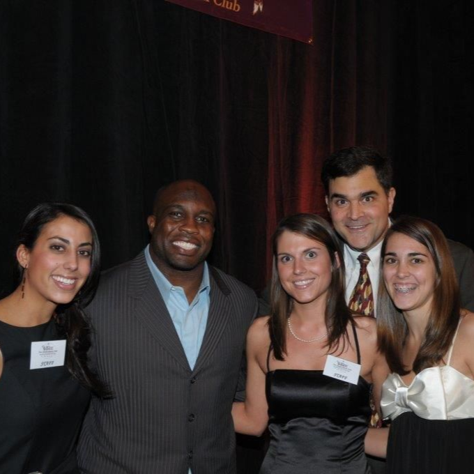 Five people posing together at an indoor event, wearing name tags and formal attire.