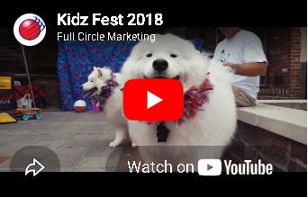 YouTube video thumbnail of a white dog in a pink lei with a red play button, titled “Kidz Fest 2018”