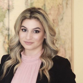 A woman in a pink shirt and black jacket is standing in front of a painting.